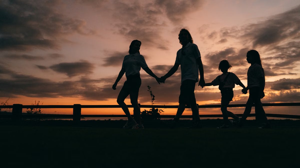 A family walks hand in hand against a vibrant sunset, evoking togetherness and peace.